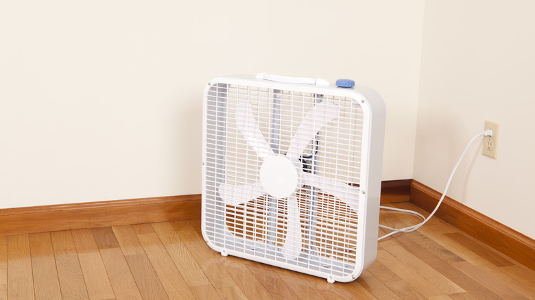 Boring white box fan sits on a hardwood floor in the corner